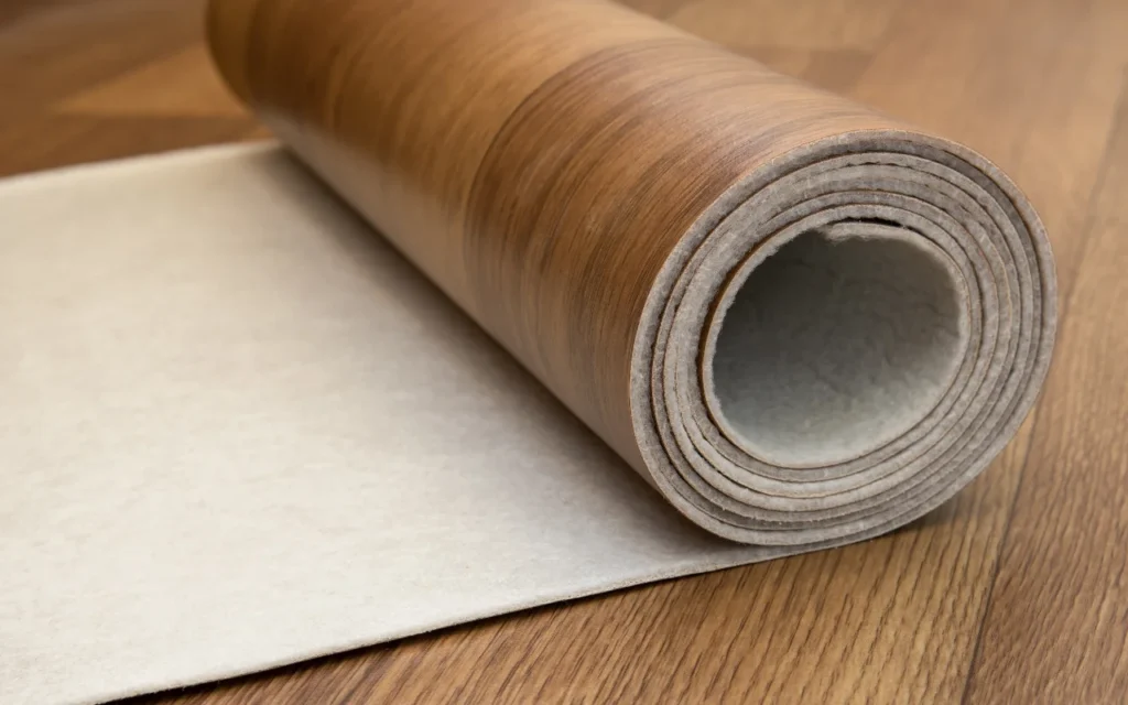 Roll of brown carpet on a wooden floor, partially unrolled to reveal backing.